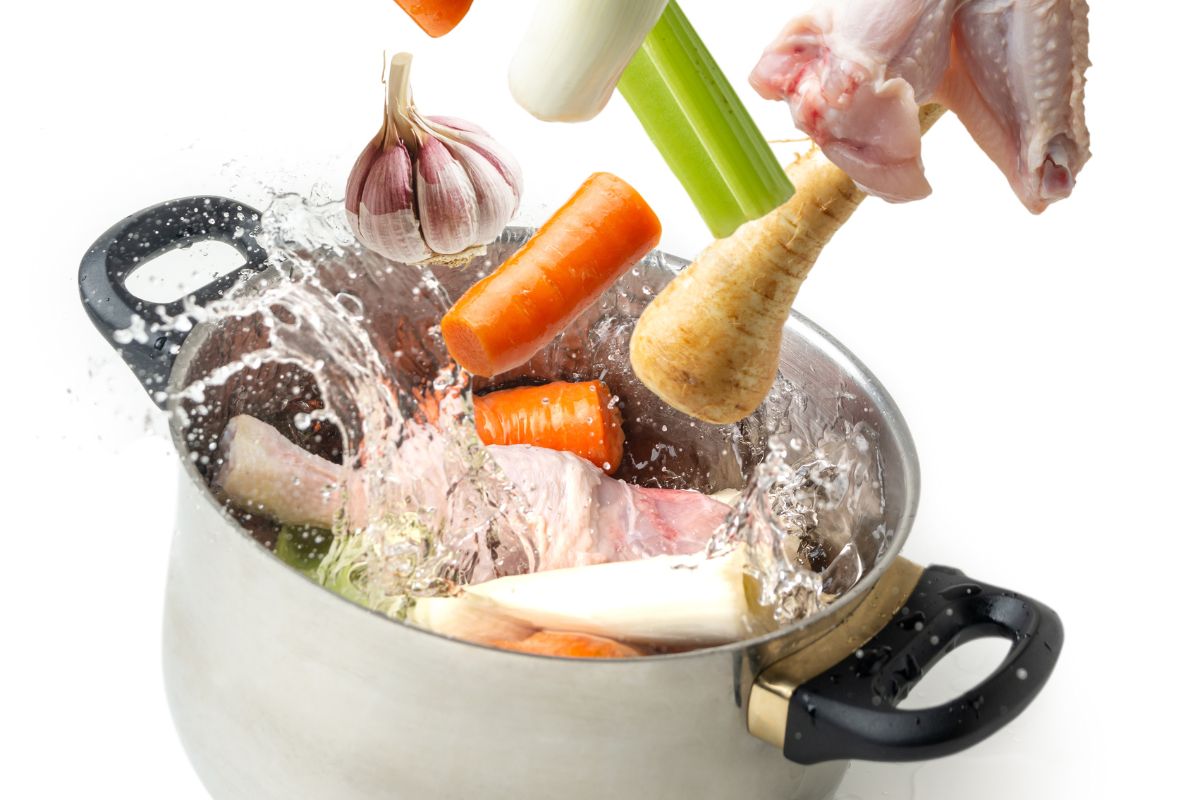 Ingredients for making broth flying towards a pot with splashing water on white background