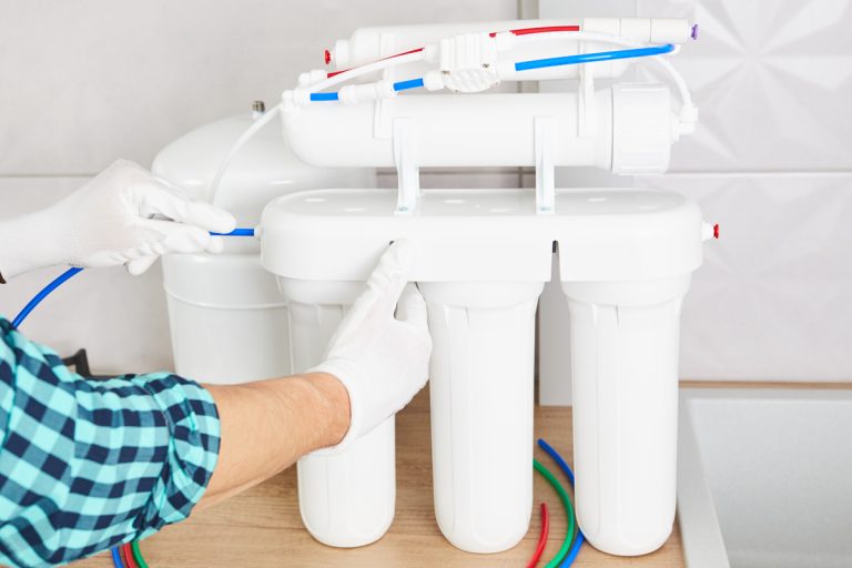 Installation purification osmosis system. Plumber or man hand replace water filter cartridges at home kitchen. Close up., How Much Does It Cost To Install A Water Filter?