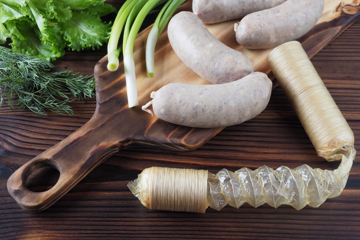 Intestines sausage casing, raw Bavarian sausages on a kitchen board, fresh greens on a dark wooden table, close-up,