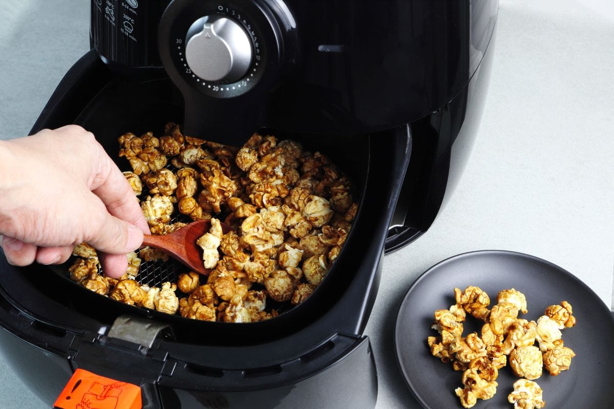 Left hand scoop the popcorn from the tray of the black deep fryer or oil free fryer appliance into the black dish on the gr