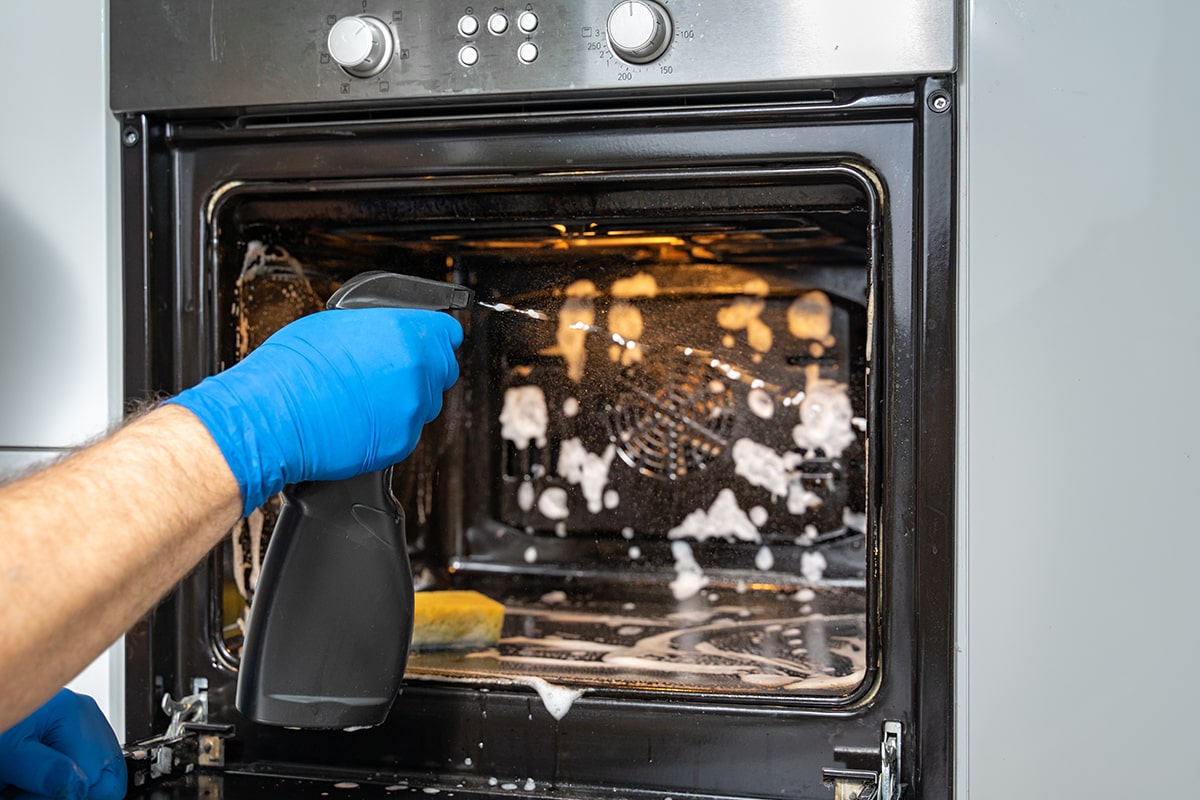 Man washes the oven with foam and a spray bottle