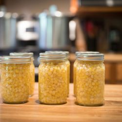 Pint jars of corn sitting on the counter ready to go in pressure canners that are sitting on the stove in the background, How To Keep Corn From Turning Brown When Canning