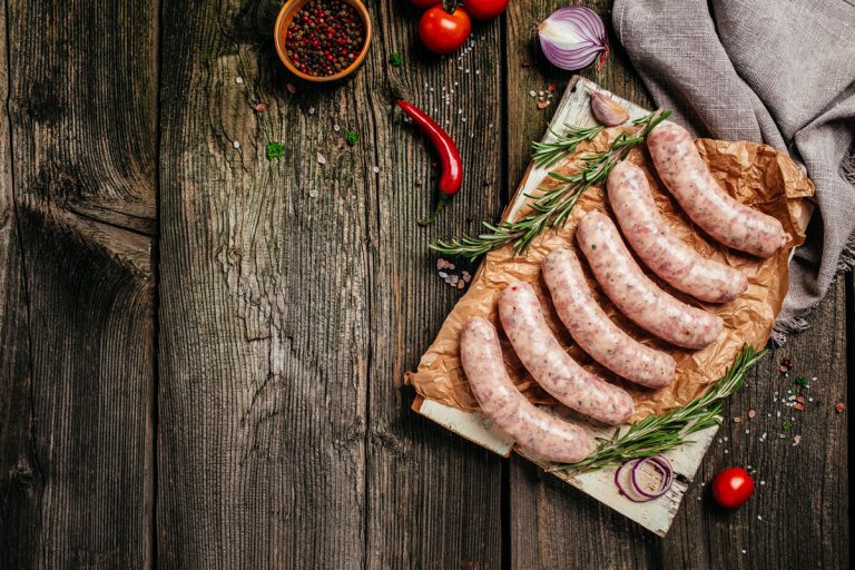 Raw stuffed sausages in cookware on a wooden, What Causes Tough Sausage Casings? [& Possible Fixes]