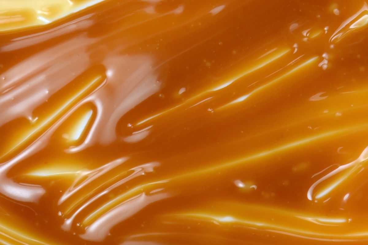 Sweet caramel sauce drop background close up. Golden Butterscotch toffee caramel liquid.