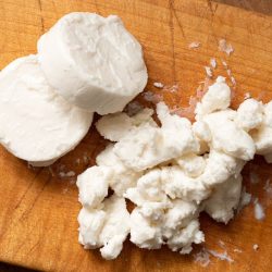 Two rounds of goat cheese and crumbled goat cheese on wood chopping board. Top view. - How To Crumble Goat Cheese