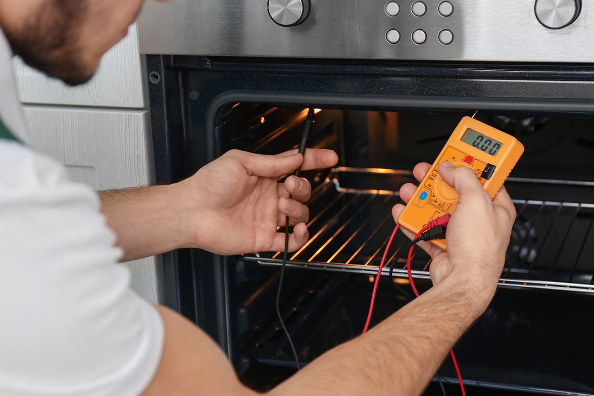 Young man with multimeter to repair the oven