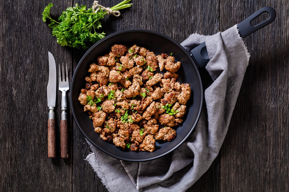 fried Italian sausage of freshly ground pork meat and spices in skillet on dark wooden table with cutlery, horizontal view from above, flat lay, close-up