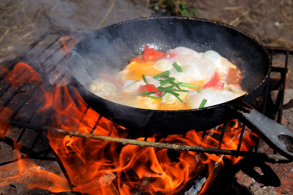 fried eggs on a campfire in the forest, fried eggs on a campfire on a camping trip, scrambled eggs in a frying pan on fire, cook an omelet on a fire, Cooking on a campfire, breakfast on the fire.