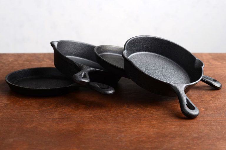 pile of cast iron skillets on old wood table. - Cast Iron Pan Doesn't Sit Flat - Why? What To Do?