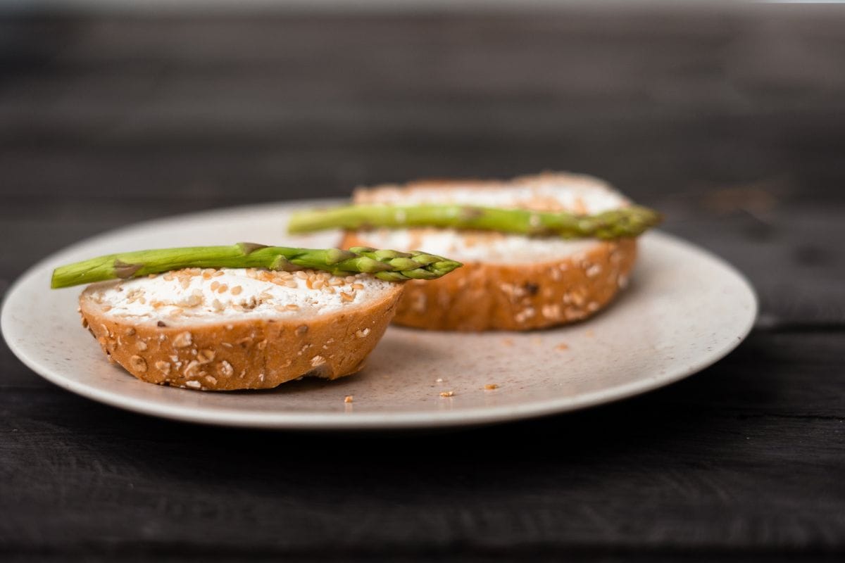 sandwich with asparagus curd cheese on a ceramic light plate on a wooden background