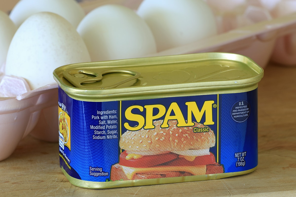 Can of unopened Spam in foreground with eggs behind