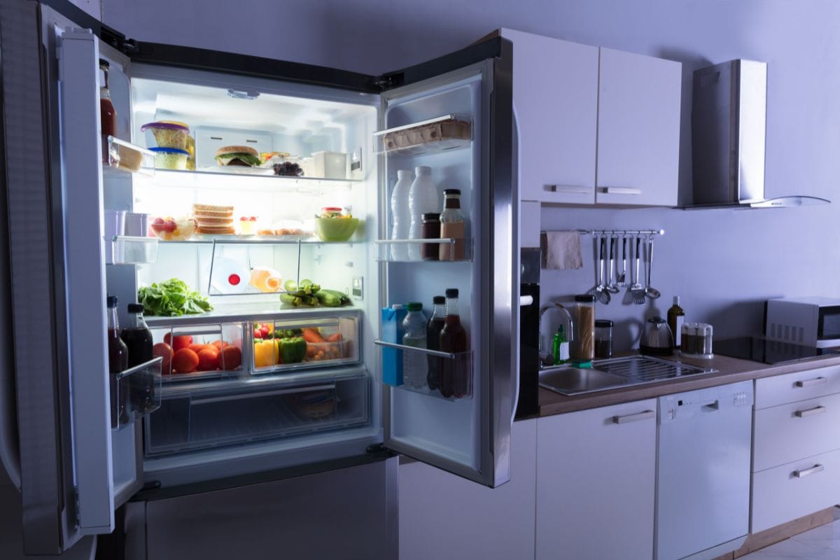 Open refrigerator full of juice and fresh vegetables in kitchen