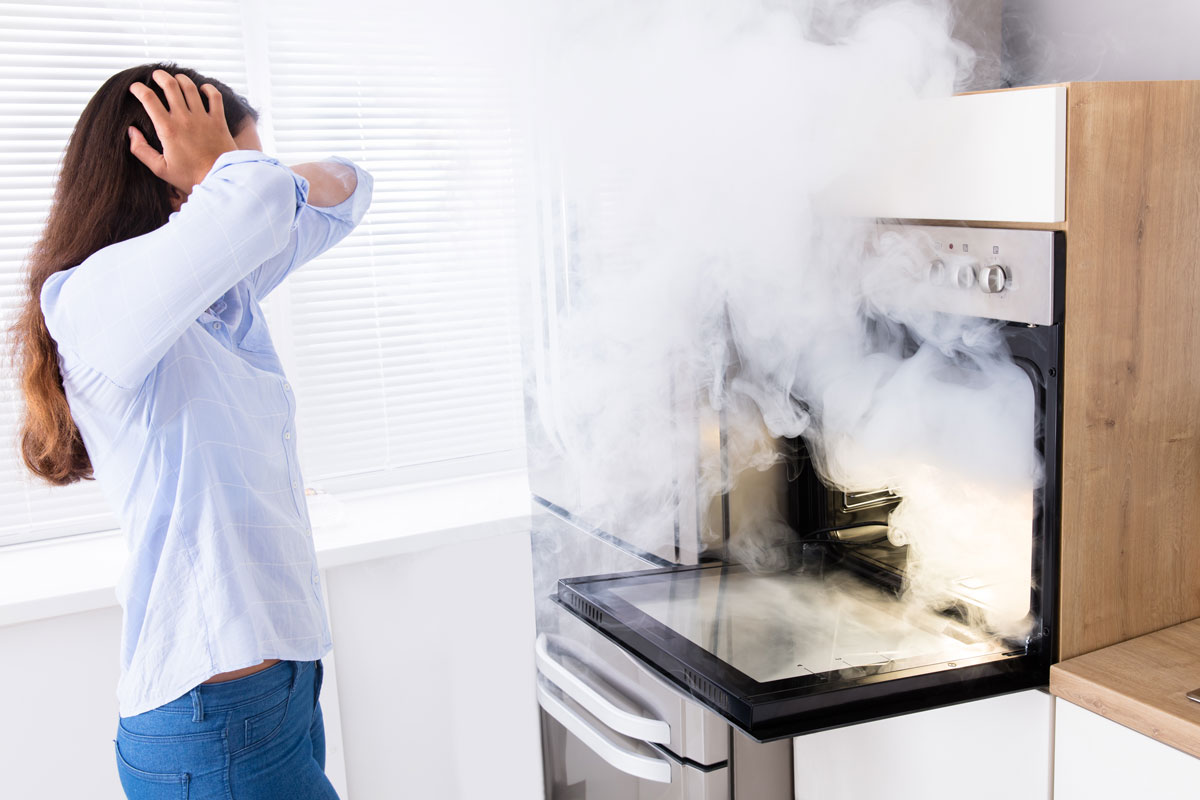 Shocked woman looking at smoke coming from oven in kitchen