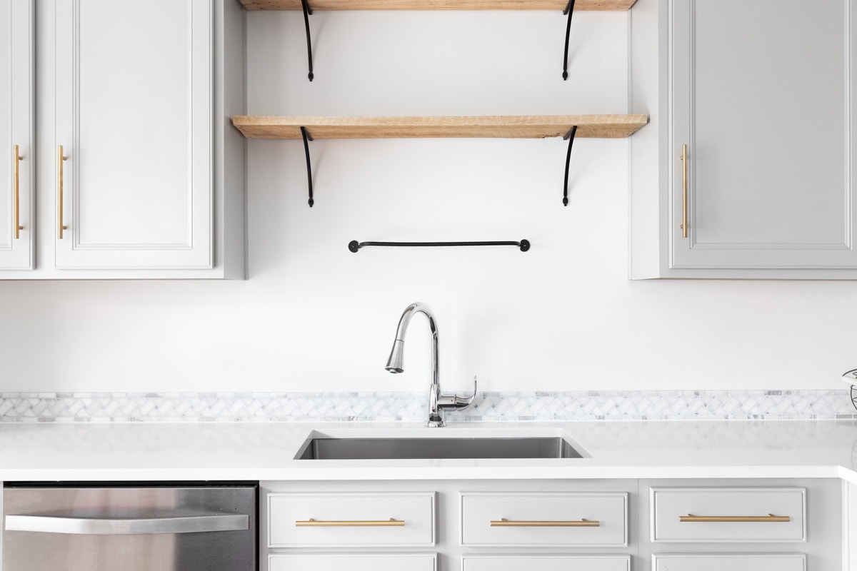 A modern farmhouse kitchen detail shot with grey cabinets, marble countertop and tiled backsplash, gold hardware, and wooden shelves., Backsplash Does Not Reach Cabinets: What To Do?