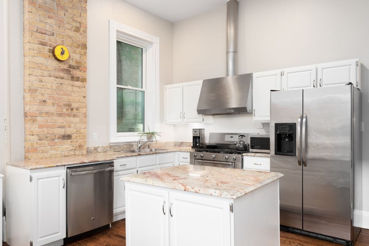  A renovated kitchen with white cabinets, stainless steel appliances, granite countertops, and a brick accent on the wall.