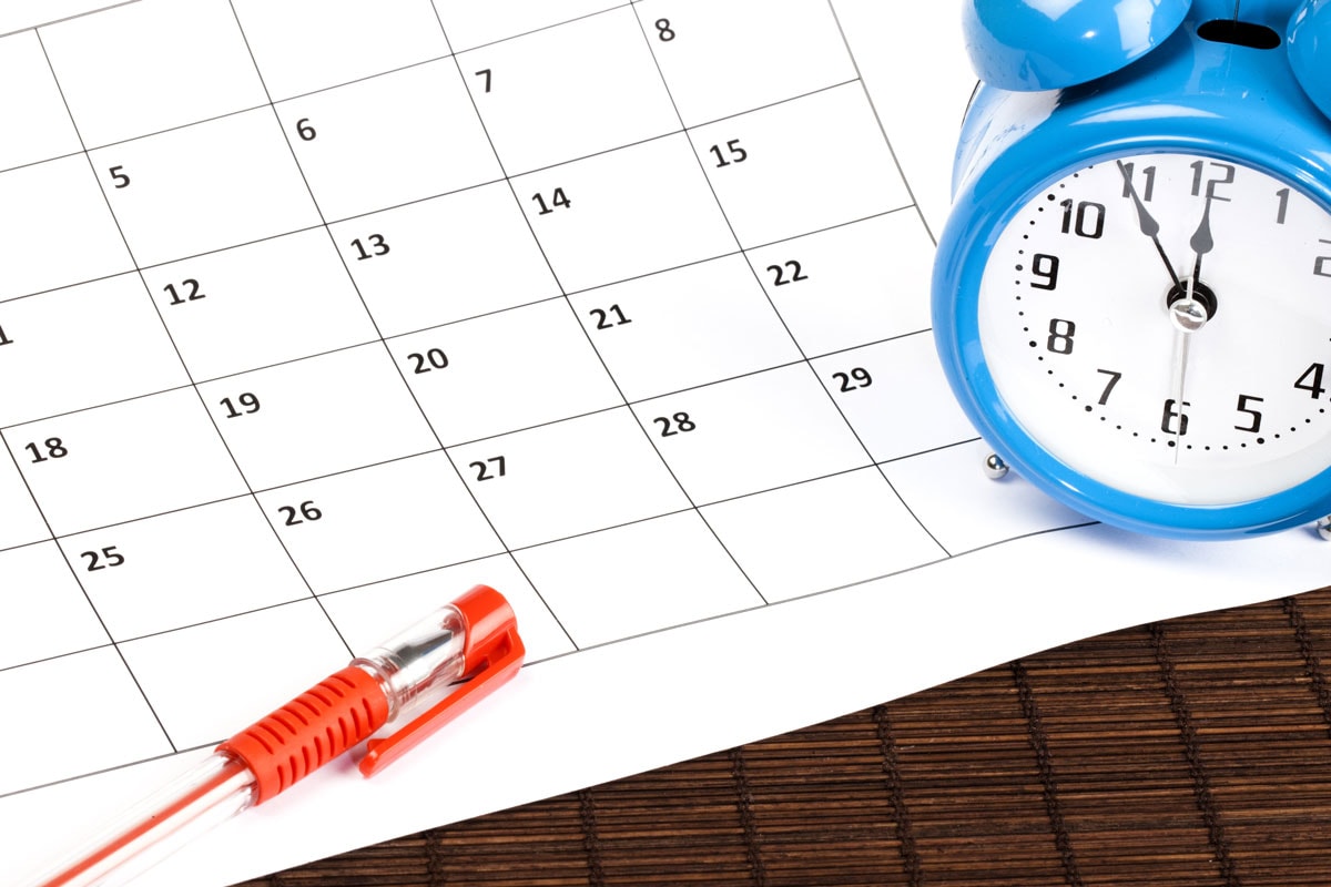 Blue alarm clock sat on a calendar with a red pen