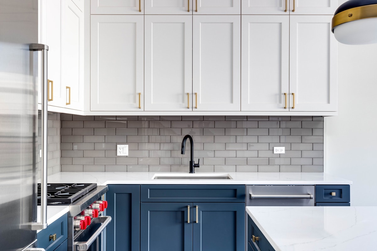Blue and white cabinets in a modern kitchen with a blue island and white granite counter top. 