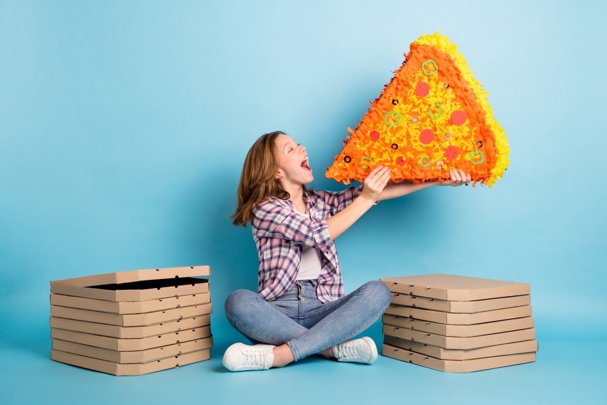 Full body photo of crazy positive pupil sit on floor hold large pizza collage open mouth isolated on blue color background
