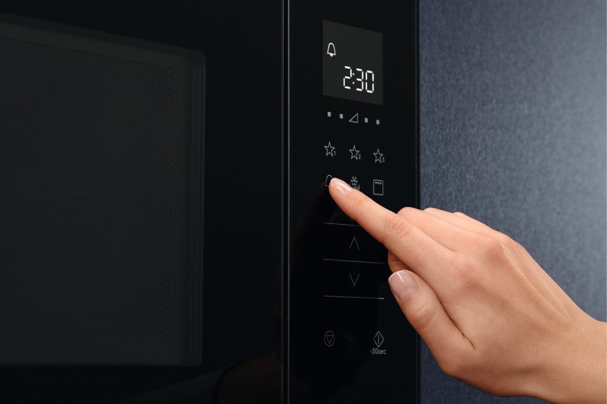 Hand pressing the button on the microwave oven