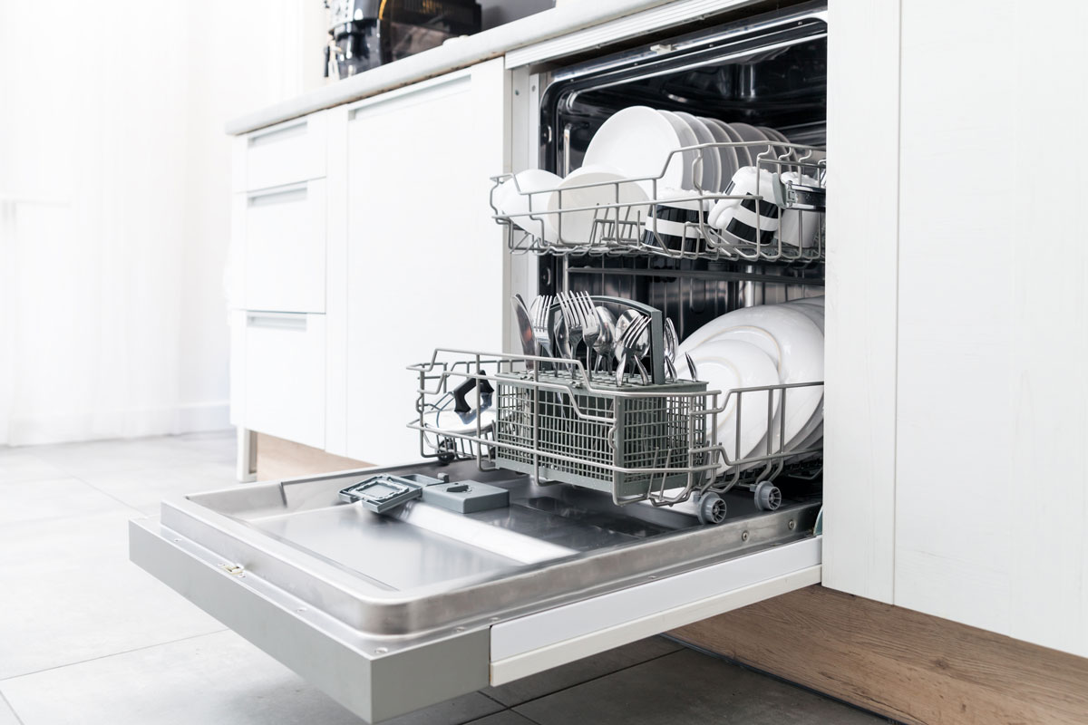 Open dishwasher with clean dishes in the white kitchen 