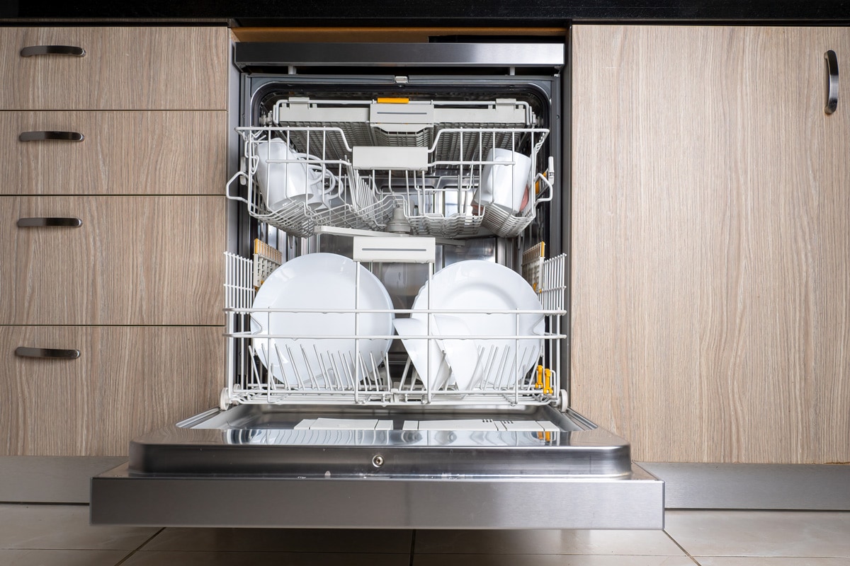 Open door of built-in dishwasher. Kitchen with integrated appliances. Plates and dishes in the dishwasher