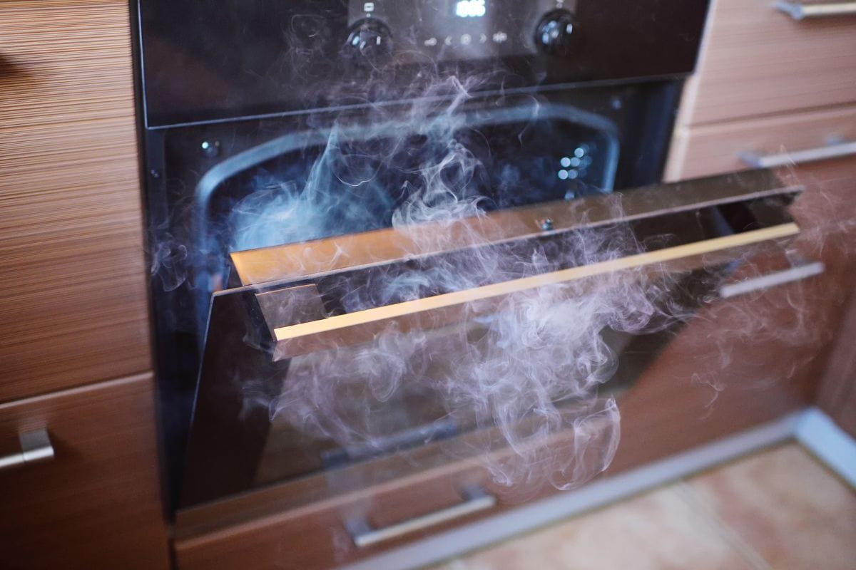 the smoke from the oven in the kitchen closeup. Burnt food.Blurred image of the oven with focus on the door handle.
