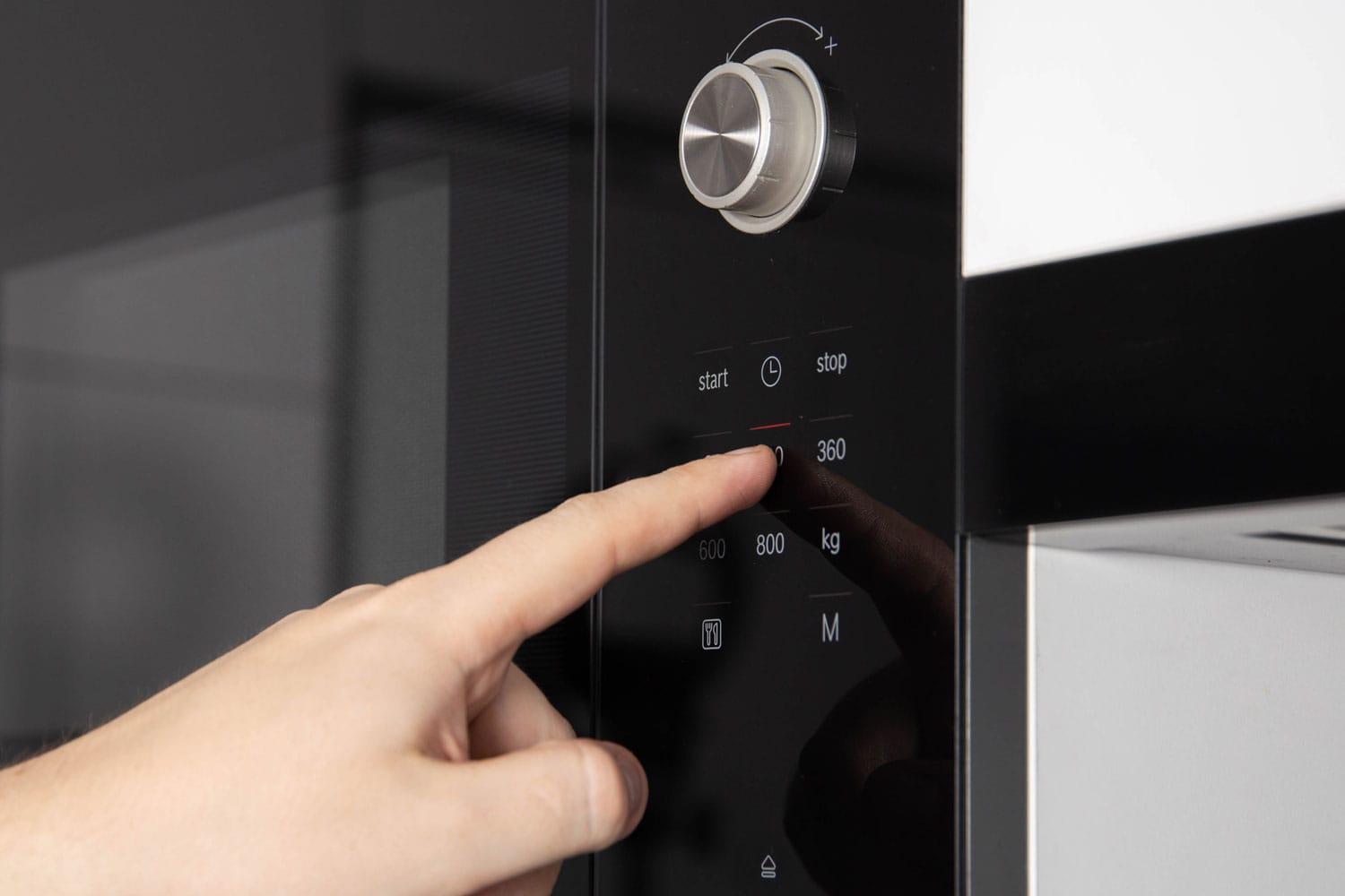 A man's hand is pressing the touch panel of a modern microwave oven to reset the Panasonic microwave.