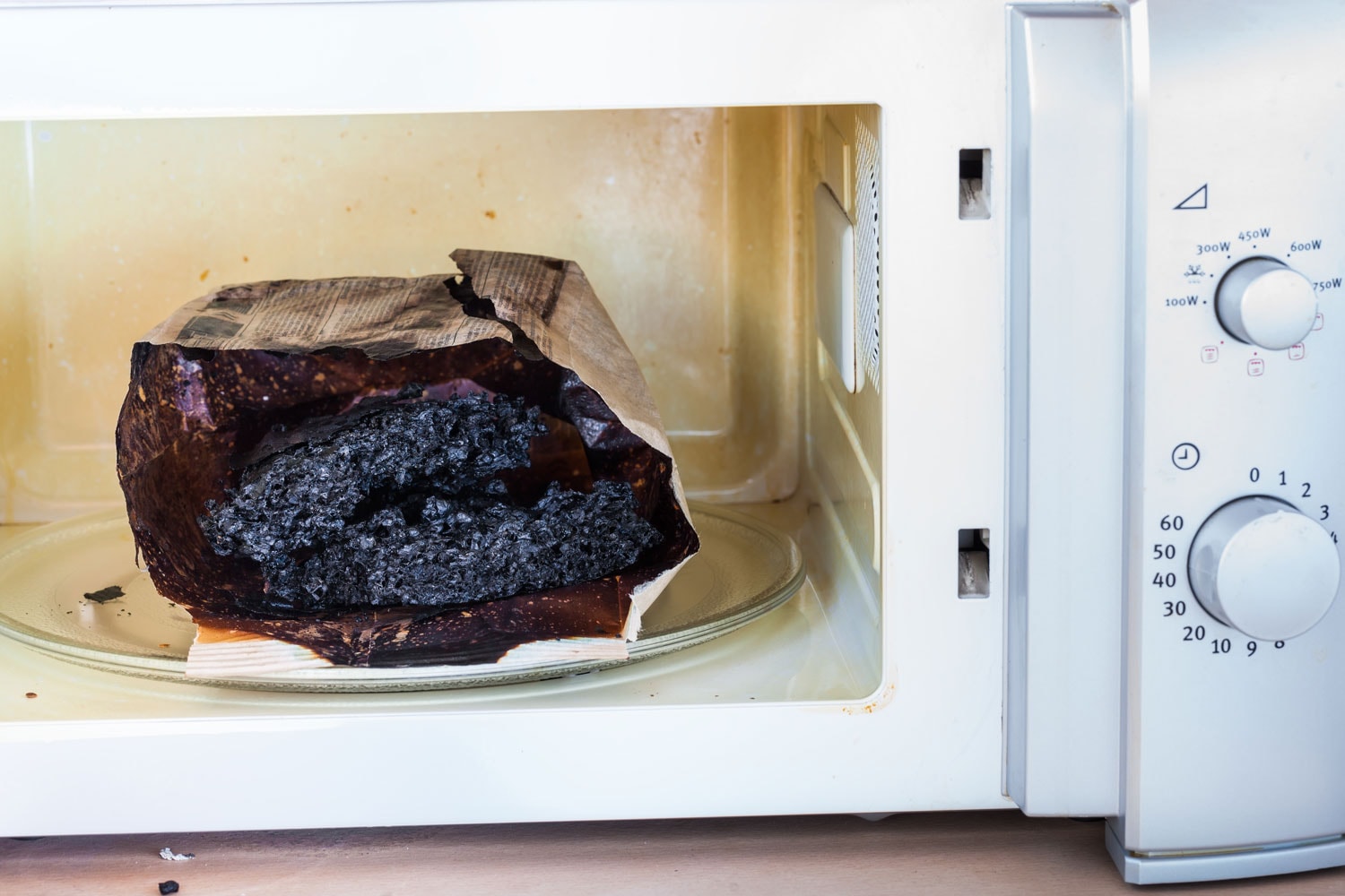 Burnt paper bag with melted and burnt popcorn in the greased and dirty microwave oven, after the explosion and fire
