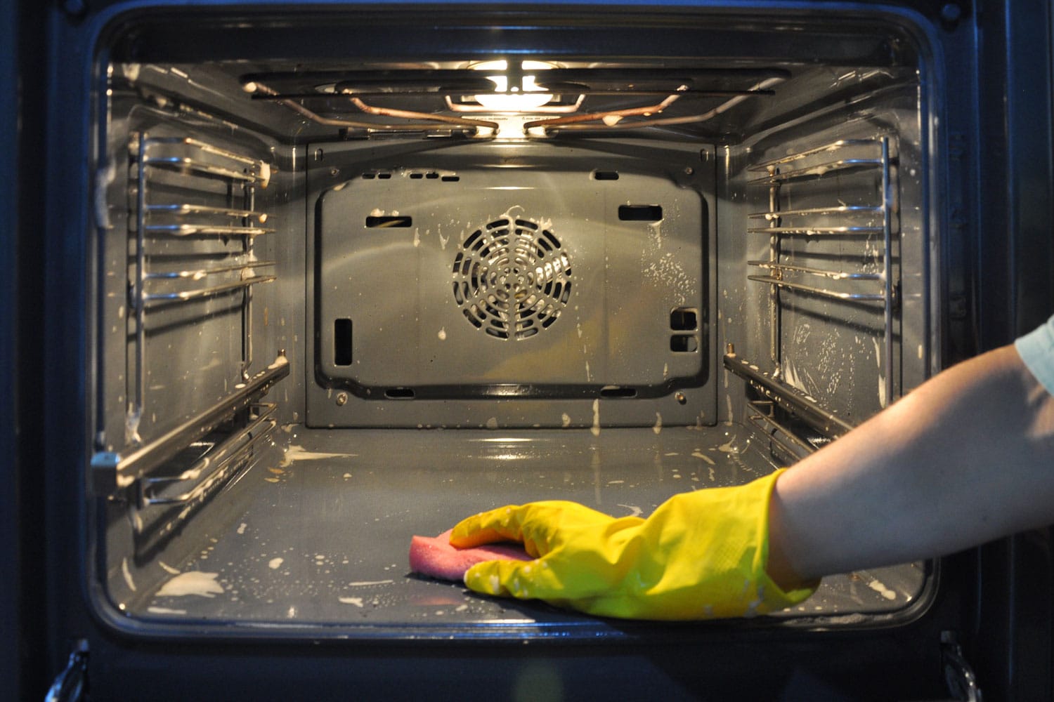 Cleaning the oven in the kitchen. hand in a yellow household glove out of focus on the background of the oven.
