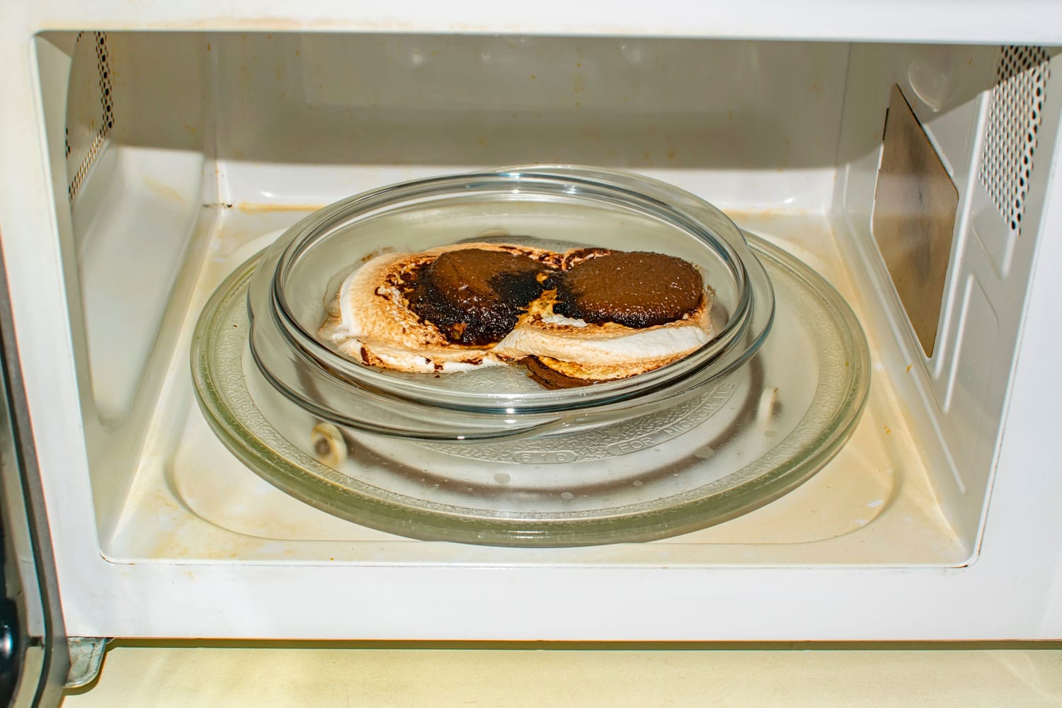 a melted bun, burnt to embers, lies on a plate in the microwave. Spoiled food, sweets
